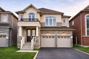 A two-story house with a front porch, a garage, and a stone facade. - 4BR Group Retreat by Canterra Stays · Sleeps 12 (Brampton)
