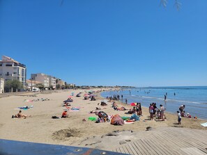 A beach with people sunbathing and swimming, buildings in the background, and a clear blue sky. - Charming 2-bedroom house: AC, rooftop terrace in the heart of enchanting Agde (Agde)
