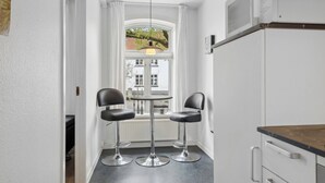 Una cocina pequeña con dos taburetes negros, una mesa redonda y una ventana que ofrece vistas a edificios.