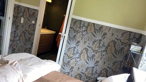 Une chambre avec deux lits, un petit bureau et un miroir. Une porte donne accès à une autre pièce.