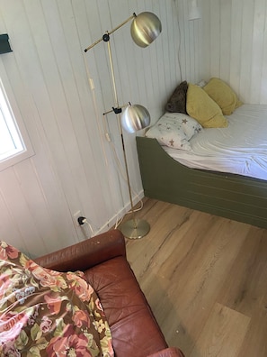 Una habitación con una cama, una lámpara de pie, un sofá de cuero marrón y un ventanal.