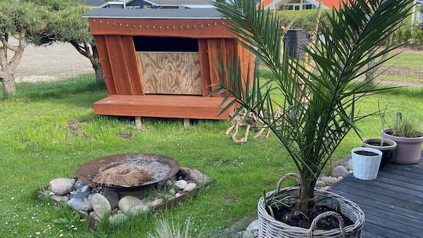 Une terrasse en bois avec un foyer, des plantes en pot et une structure en bois en arrière-plan.