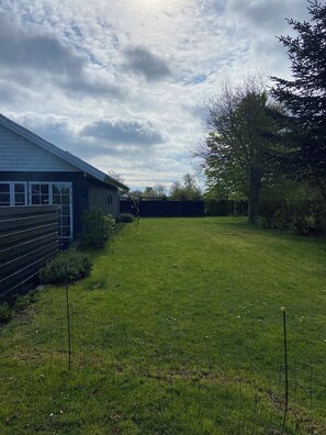 A grassy yard with a building on the left, a fence, and trees in the background. - Lovely holiday home near Funens beautiful nature (Otterup)