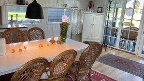 Un espace repas comprenant une table, des chaises, un luminaire suspendu et une vue à travers une porte vitrée.