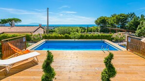 Eine Holzterrasse mit Schwimmbad, Liegestühlen und Blick auf das Meer.