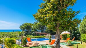 Ein Poolbereich mit Liegestühlen, einer Pergola und Blick aufs Meer.