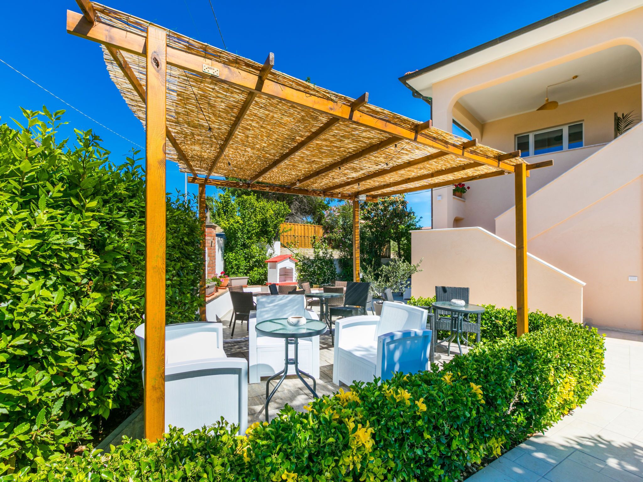 Un espace extérieur aménagé en terrasse, avec des meubles blancs, une pergola et un four en briques.