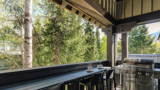 Un área de cocina al aire libre con una parrilla de acero inoxidable, dos taburetes negros y una mesa de madera.