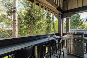 Un área de cocina al aire libre con una parrilla de acero inoxidable, dos taburetes negros y una mesa de madera.