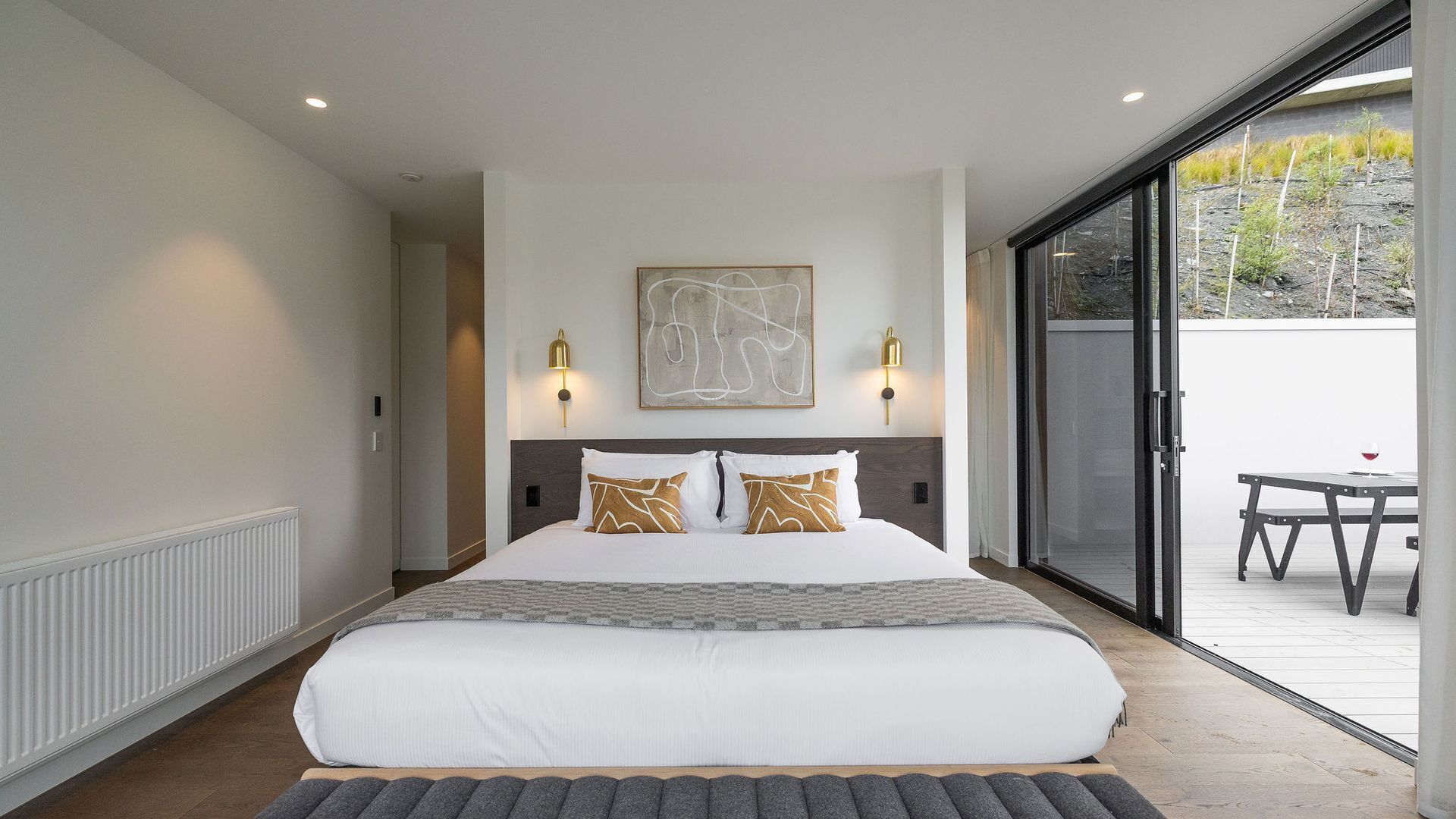 Une chambre moderne avec un grand lit, deux lampes fixées au mur et une vue sur l’extérieur grâce à une porte-fenêtre coulissante.