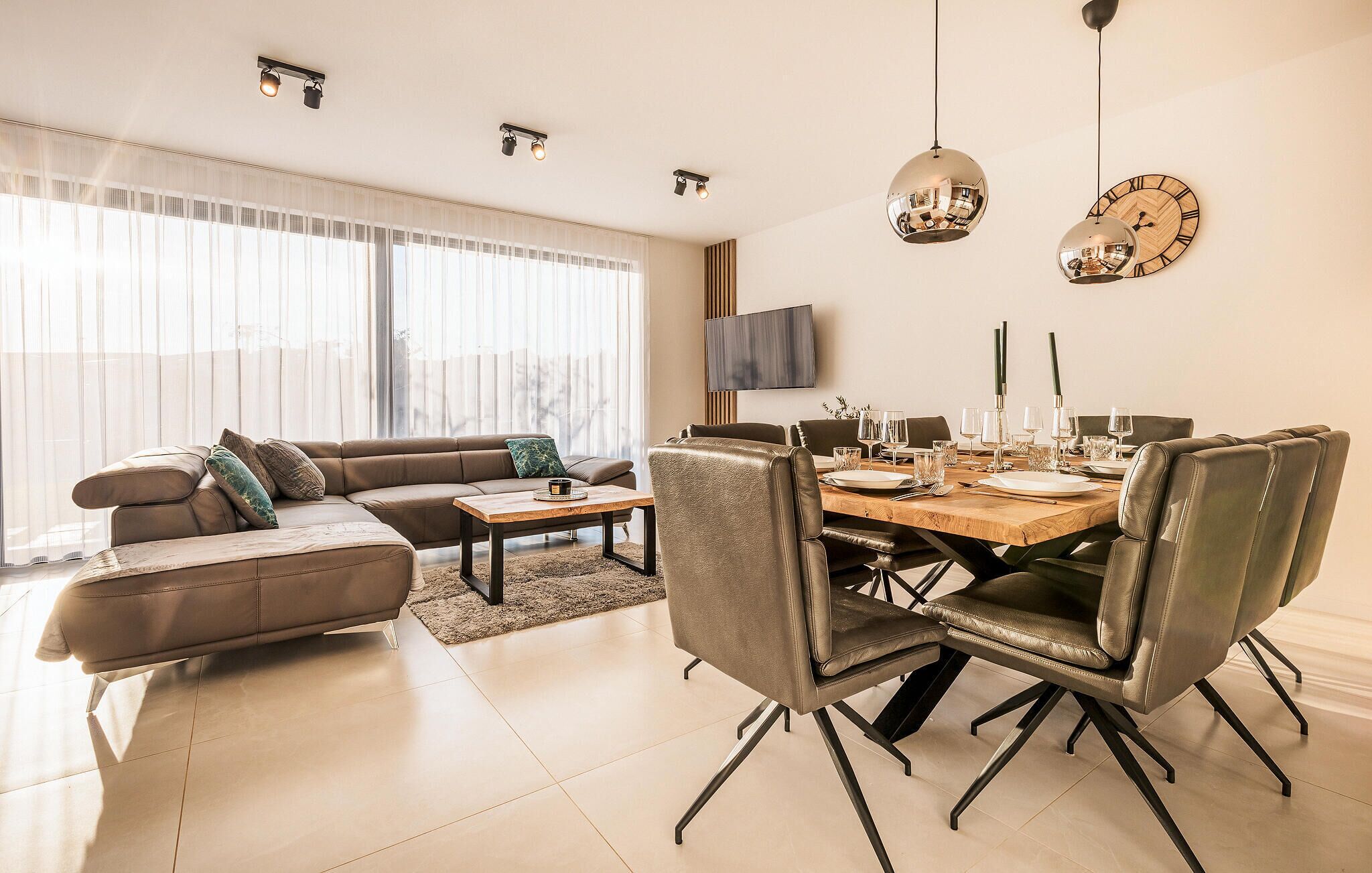 Un salon moderne avec un canapé, une table à manger dressée pour six personnes et un téléviseur fixé au mur.