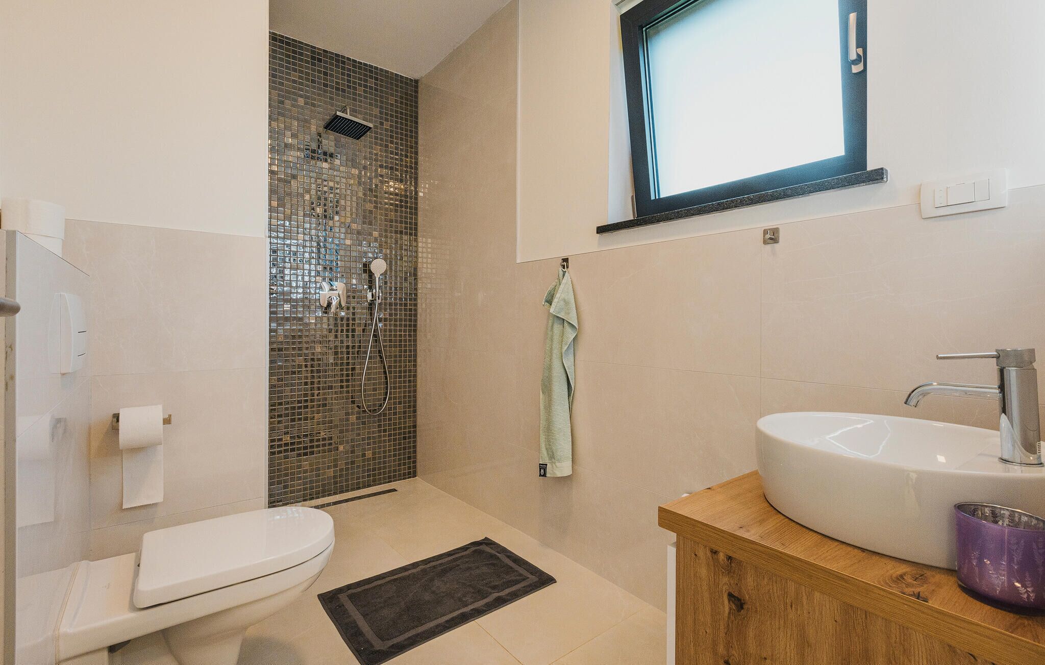 A modern bathroom with a toilet, shower, sink, and a small window.