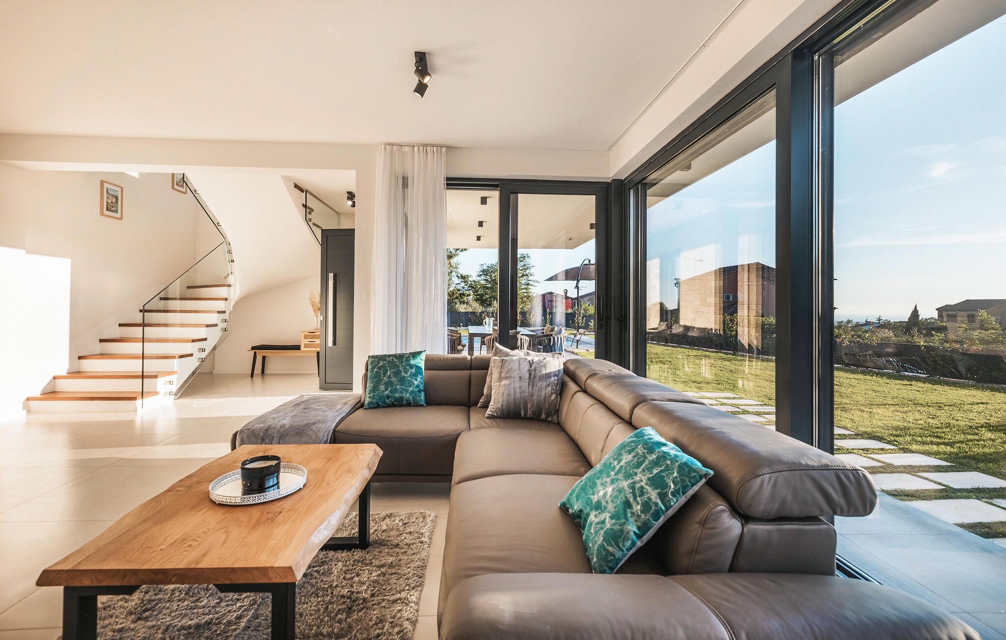 Uma sala de estar moderna com um amplo sofá modular, uma mesa de centro de madeira e uma escada que leva a um andar superior.