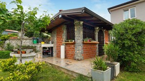 Un petit bâtiment en pierre, doté d’une cheminée en briques, d’un banc en pierre et de plantes en pot.