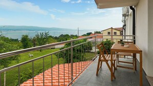 Un balcon donnant sur un plan d’eau et des collines, une table et une chaise en bois, ainsi qu’une balustrade.