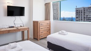 Ein Hotelzimmer mit großem Fenster, Flachbildfernseher, Schreibtisch aus Holz und zwei Betten.