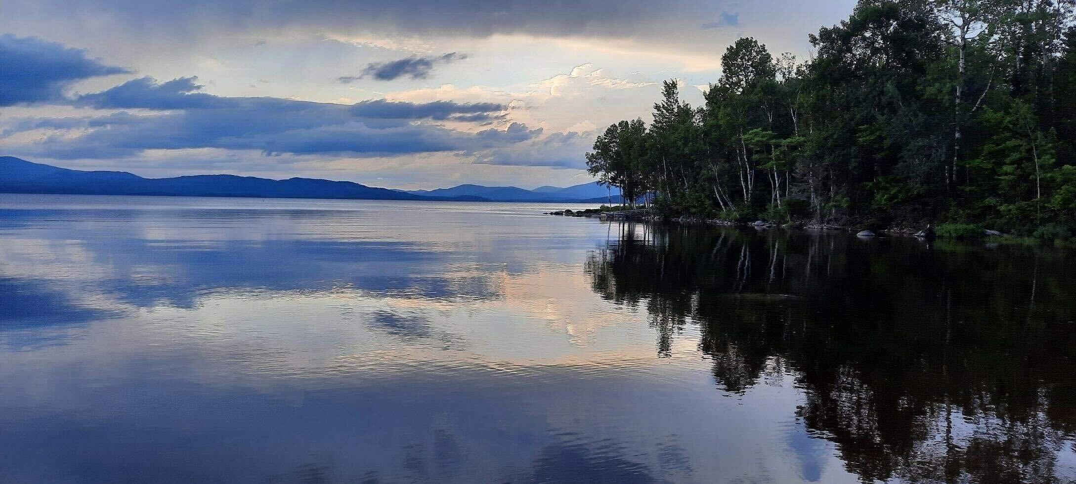 A calm lake with a forested shoreline and distant mountains.