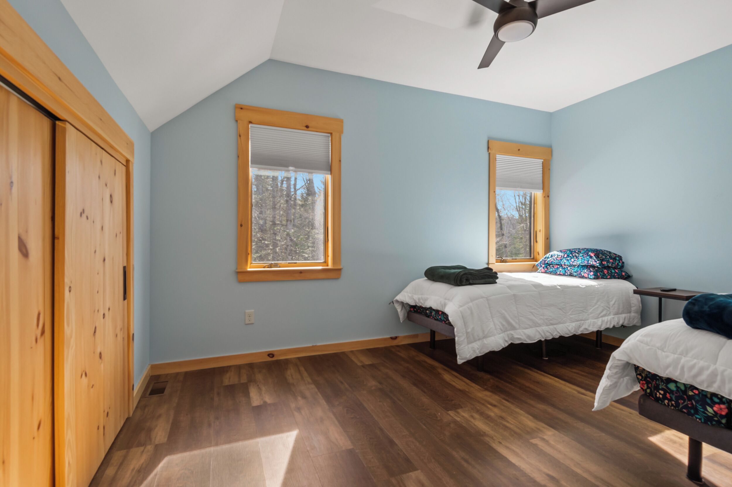 A bedroom with two beds, wooden flooring, and a ceiling fan.