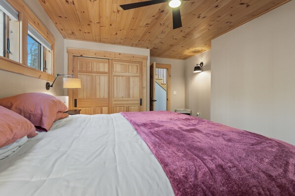 A bedroom with a wooden ceiling, a bed with white and pink bedding, and a purple throw blanket.