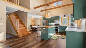 Cocina amplia con piso de madera, una isla central y muebles de color verde.