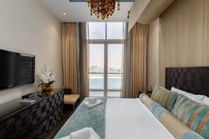 A modern hotel room with a large bed, a sofa, a TV, and a view of the city and water.