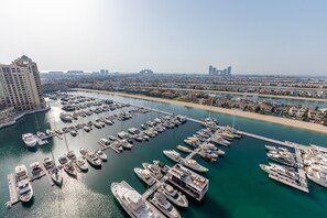 A marina with numerous boats docked, a large building on the left, and a bridge connecting to the mainland.