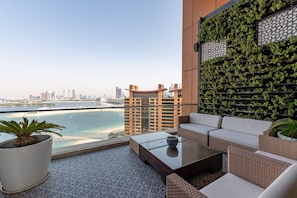 Un balcón con vistas a un horizonte urbano y una masa de agua. Hay una zona de estar con un sofá y una mesita de centro.