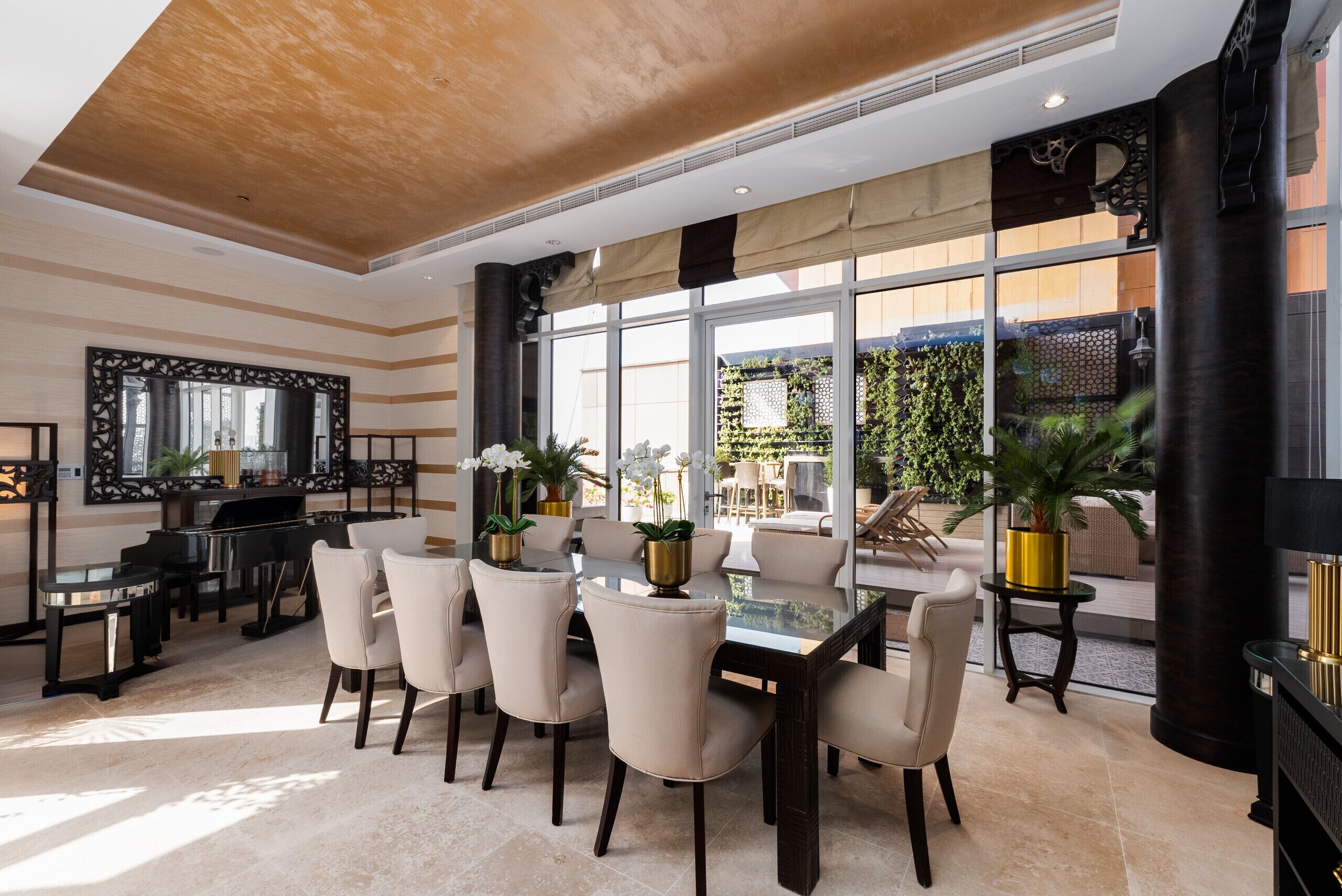Un vaste espace dédié à la salle à manger, avec une table en verre, des chaises de couleur beige et un piano.