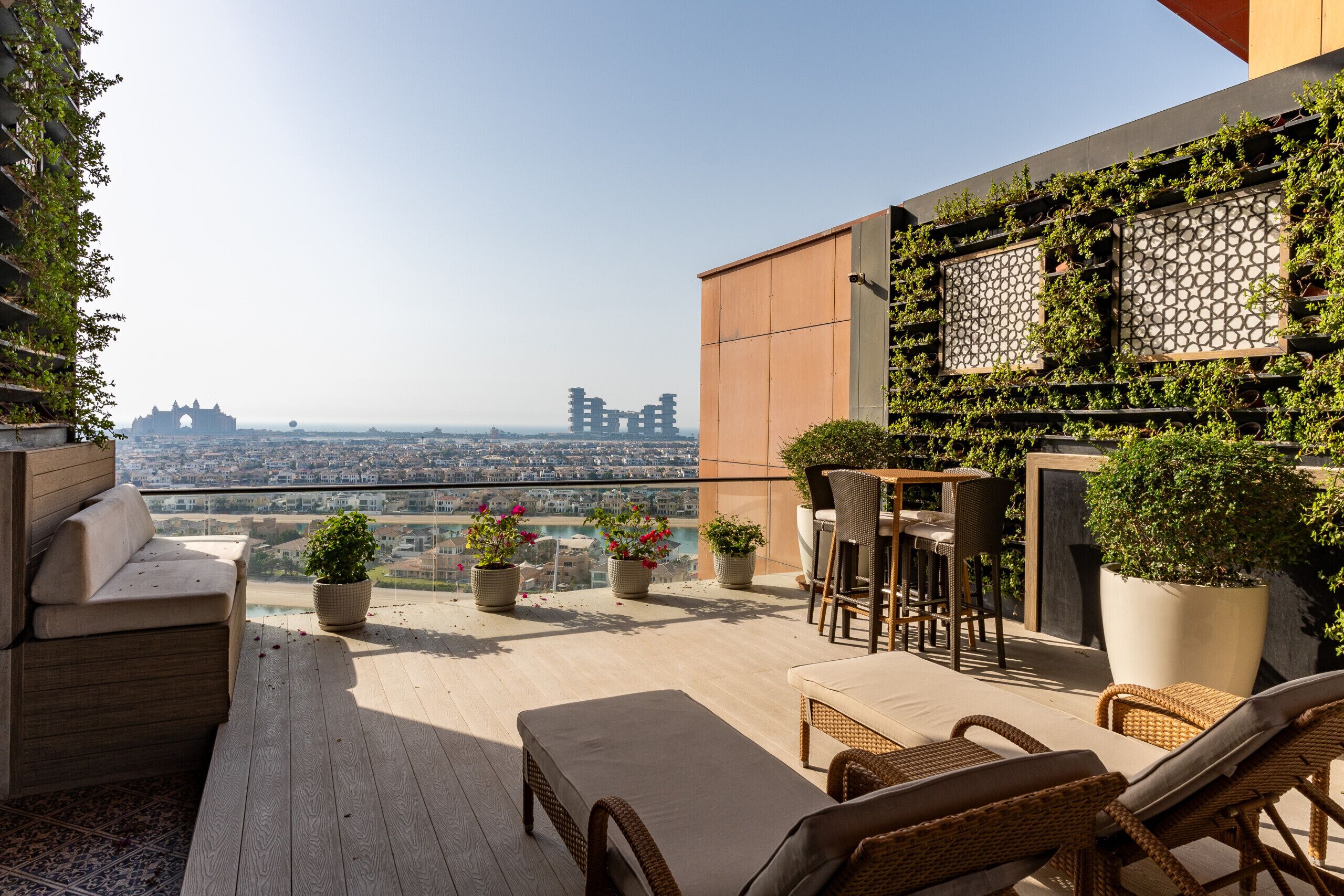 Eine Dachterrasse mit Sitzgelegenheiten im Freien, Topfpflanzen und Blick auf die Stadt.