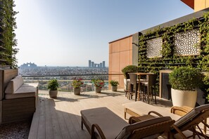 Une terrasse sur le toit, aménagée avec des espaces de détente en plein air, des plantes en pot et offrant une vue sur le paysage urbain.