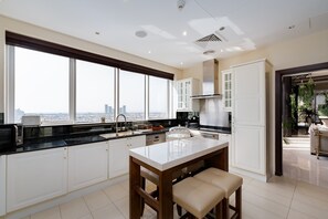 Una cocina moderna con una isla grande, armarios blancos y vistas de la ciudad a través de amplios ventanales.