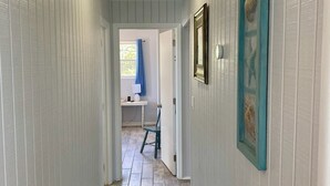 Un pasillo estrecho con paredes blancas empapeladas, suelo de madera y una puerta que da a una habitación con cortina azul.