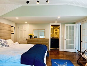 A bedroom with a bed, dresser, mirror, and a view into the bathroom.