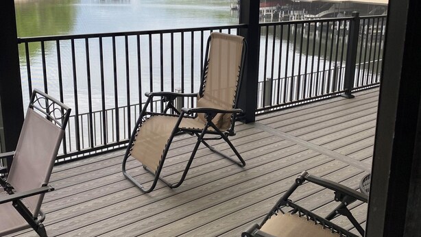 Een houten terras met twee stoelen en een tafel, met uitzicht op een rivier met gebouwen en begroeiing op de achtergrond.