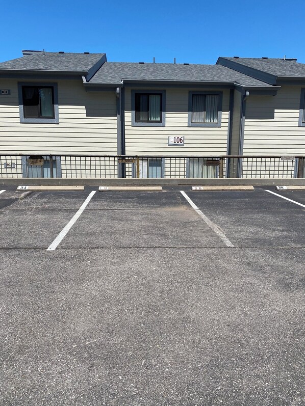 Un edificio con un letrero del número 106, un estacionamiento con espacios demarcados y una cerca.