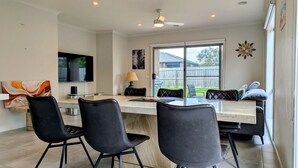 A modern kitchen with a dining area, featuring a large window, a ceiling fan, and a dining table with chairs. - Spacious home near Bellarine Peninsula Trail (Curlewis)