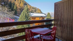 Una terraza de madera con una mesa y sillas, con vistas a un paisaje montañoso.