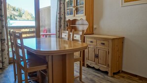 Un comedor con una mesa y sillas de madera, un mueble con cajones y vistas a través de un ventanal.