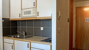 Una cocina compacta con armarios blancos, un microondas, un fregadero y una estufa.