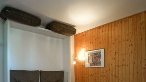 Una cama con colchón blanco y cabecera gris en una habitación con paredes de madera y una mesita de noche.
