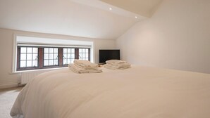 A bedroom with a large bed, a window with blinds, a flat-screen TV, and a radiator. - 57A Thoroughfare, Woodbridge (Woodbridge)