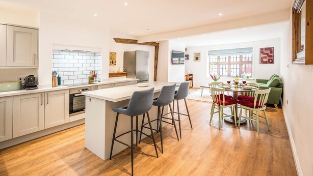 A modern kitchen with a central island, bar stools, and a dining area with a table and chairs. - 57A Thoroughfare, Woodbridge (Woodbridge)