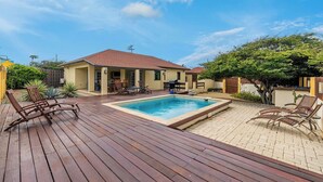 Una casa con piscina, terrazza in legno e mobili da esterno.