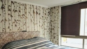 Un lit recouvert d’une couvre-lit à rayures, un mur orné d’un motif de bouleaux et une fenêtre avec un store foncé.