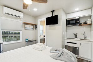 Een moderne hotelkamer met een bed, een flatscreen televisie, een kitchenette en een badkamer, zichtbaar door een geopende deur.