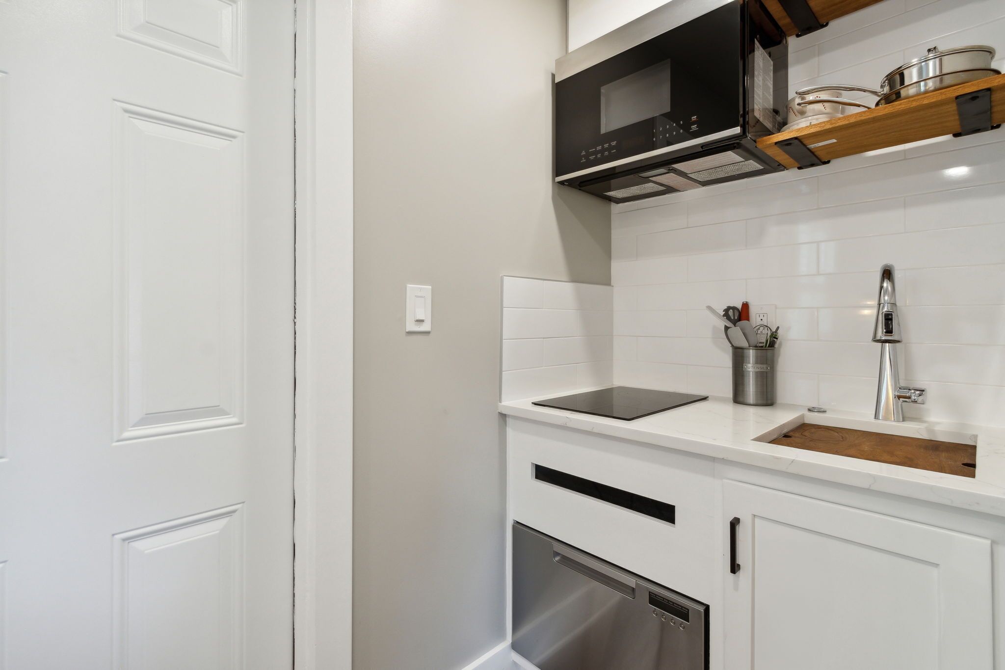 A kitchen with white cabinetry, a black microwave, and a stainless steel sink.