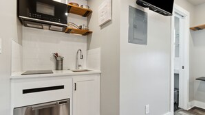 A modern kitchen with white cabinetry, a stainless steel dishwasher, a microwave, and wooden shelves above the counter. - Luxury Studio • Steps to Beach • Kitchenette • Outdoor Seating (Fernandina Beach)