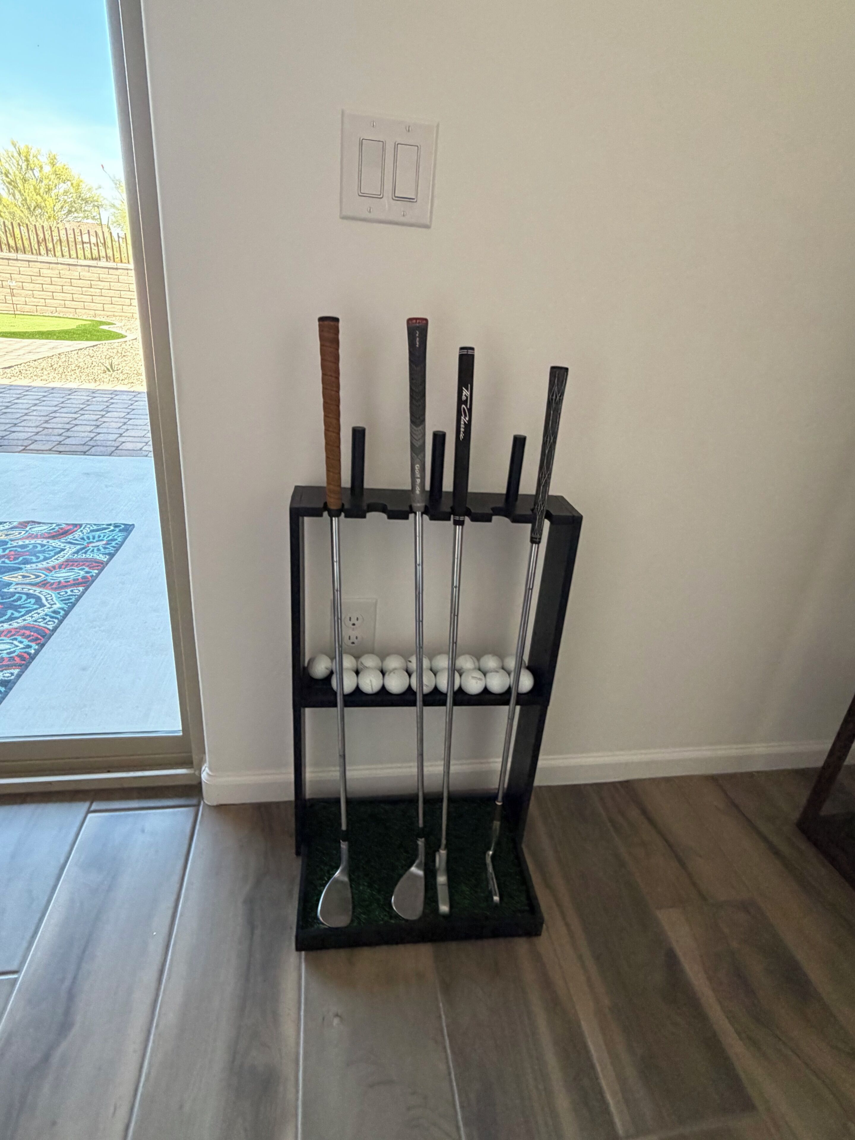 A rack with golf clubs and balls in a room with a wooden floor and a door leading outside.