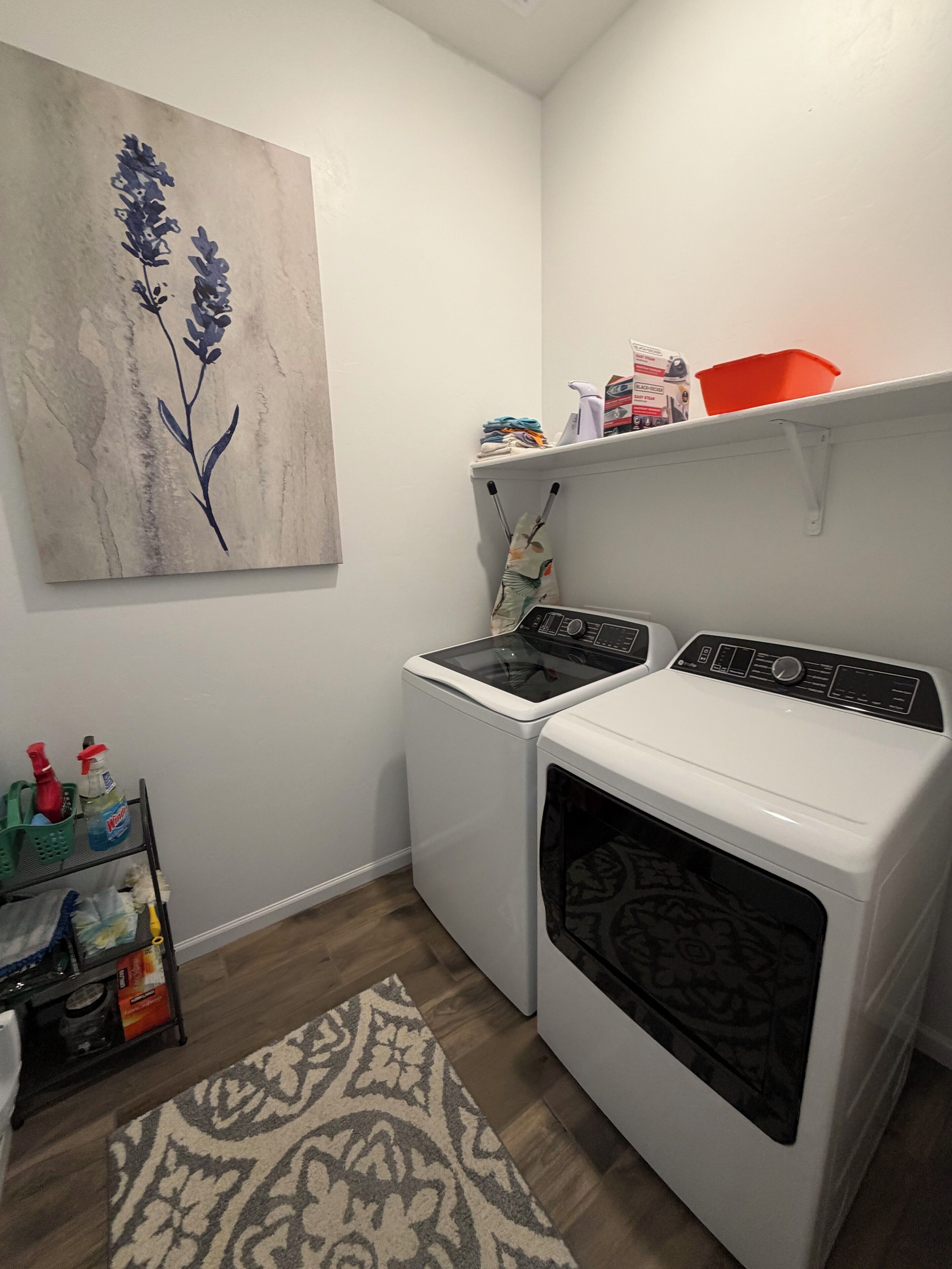 Un espace buanderie comprenant un lave-linge, un sèche-linge et une étagère où sont rangés les produits de nettoyage.
