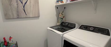 Un espace buanderie comprenant un lave-linge, un sèche-linge et une étagère où sont rangés les produits de nettoyage.